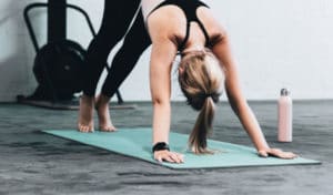 Young blonde woman does downward dog yoga position on a teal yoga mat | Nutrition Blog | Starting an Exercise Routine