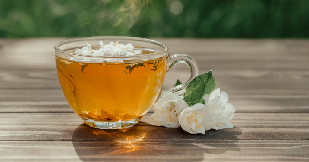 Chamomile Tea sits steaming in a clear mug surrounded by white, delicate chamomile flowers.