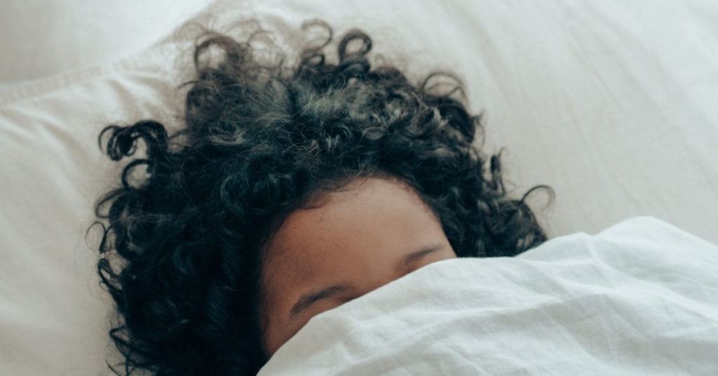 Woman's forehead and eyebrows poking out from under a large white comforter as she sleeps | Lack of sleep and weight gain
