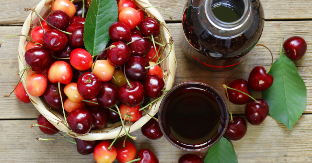 A birds-eye-view of a bowl of ripe cherries set next to a glass and jar of cherry juice.