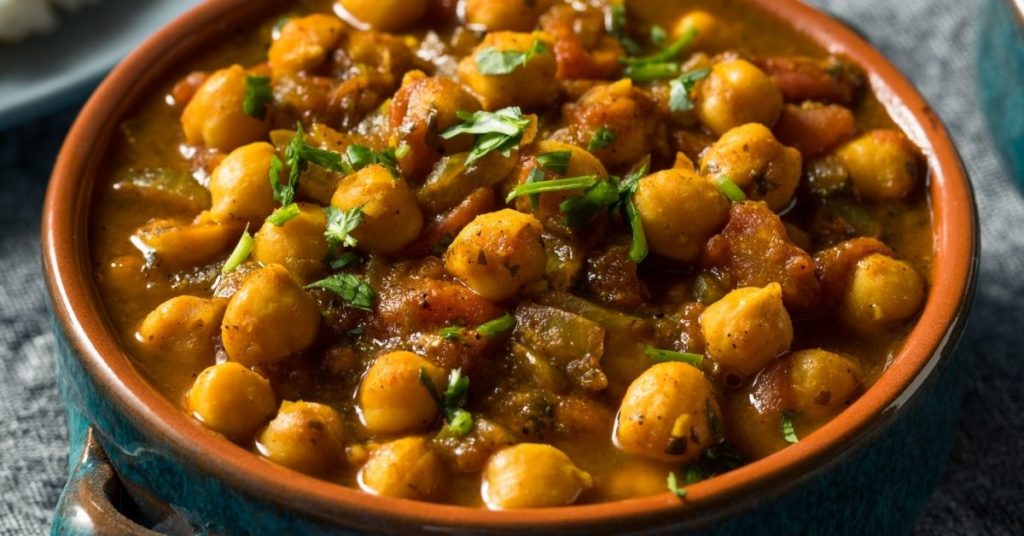 Chickpeas sit in a dark curry sauce garnished with bits of herb