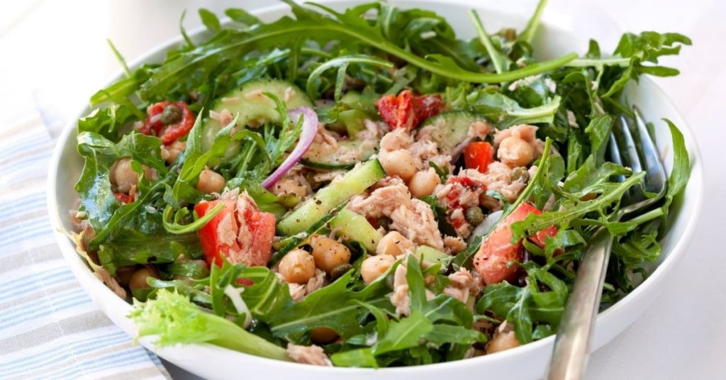Tuna, cucumber, tomatoes, and chickpeas top a large bed or arugula