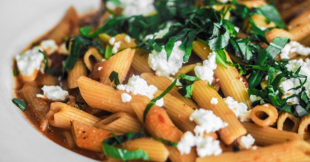 A full dish of pasta with a red sauce, topped with feta cheese and fresh herbs