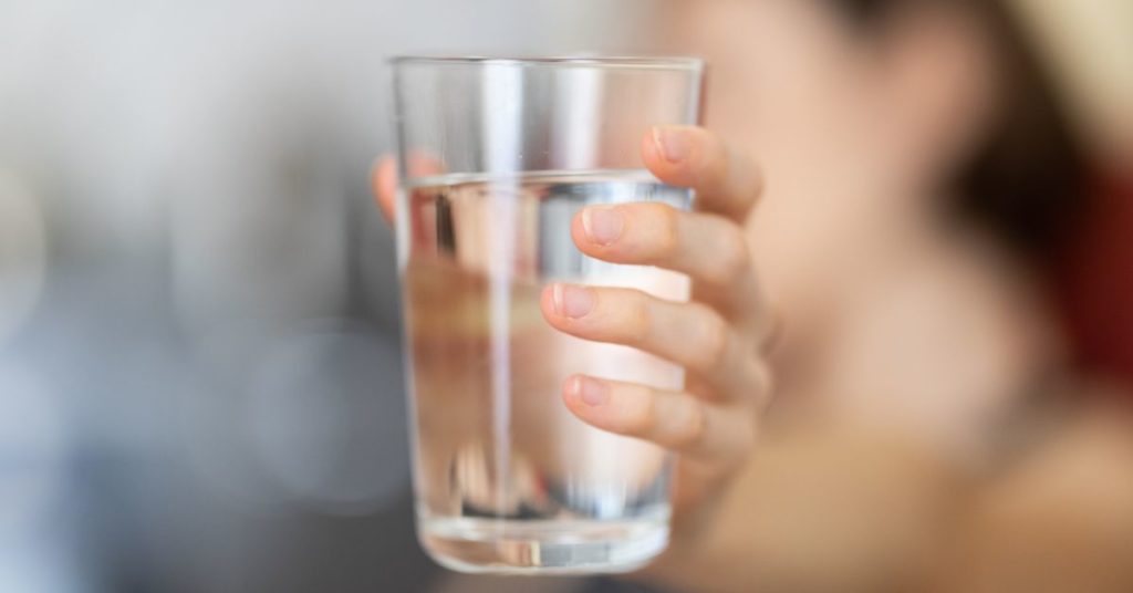 A womans hand holds out a glass of water