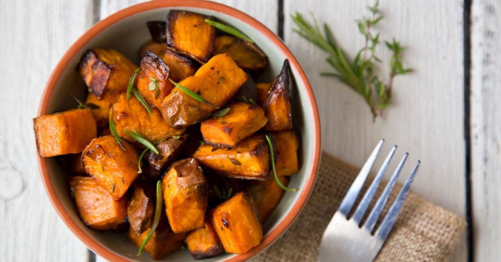 Diced and roasted carmelized sweet potato rests in a bowl and garnished with fresh rosemary