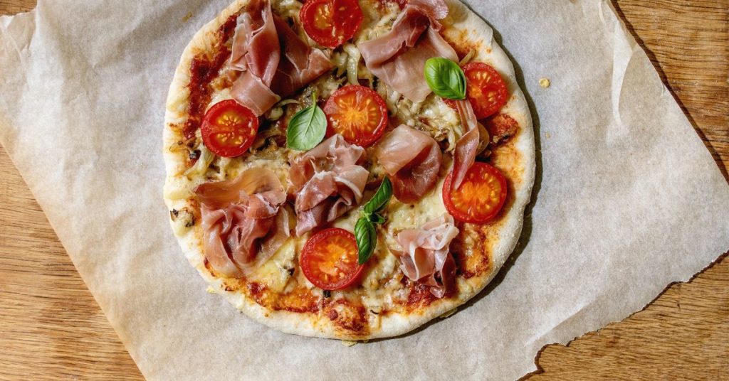 A fresh homemade pizza topped with basil, tomatoes and prosciutto on parchment paper