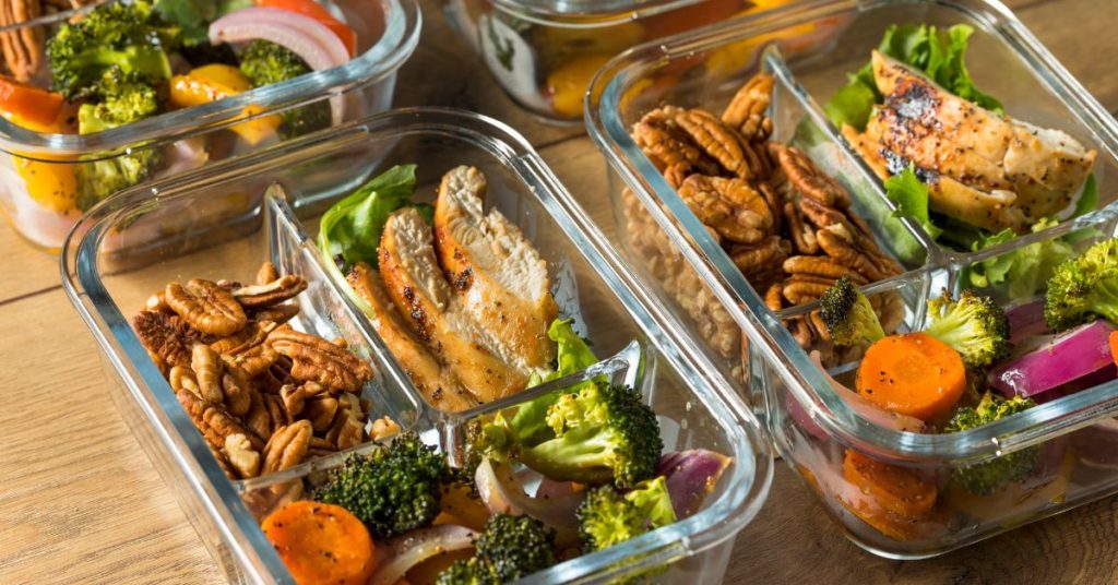 Several glass containers line the countertop, each with divided pre-portioned areas, filled with healthy foods, like walnuts, chicken, and roast vegetables, Meal Prep Ideas for Weight Loss