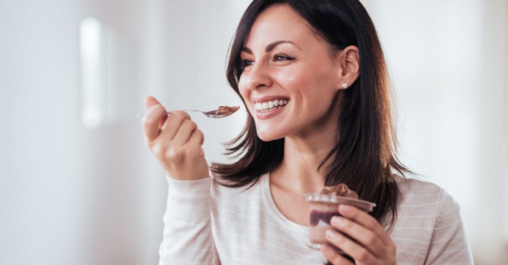 A happy smiling woman delicately holds up a small spoonfull of a chocolate mousse dessert, mindful eating for weight loss