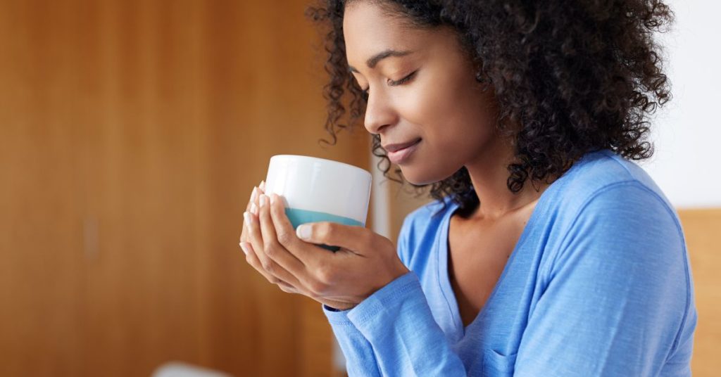 A woman slowly, peacefully smells her cup of tea