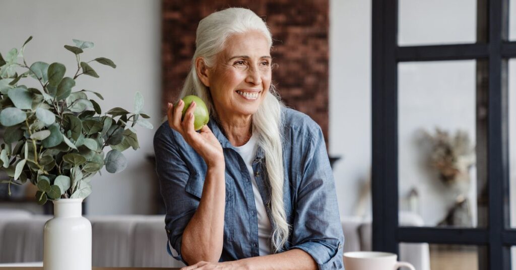 A white-haired woman holds up an apple she's about to eat