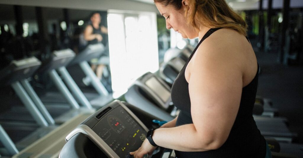 Plus-sized woman starts up a treadmill at a gym at the beginning of her weight loss journey
