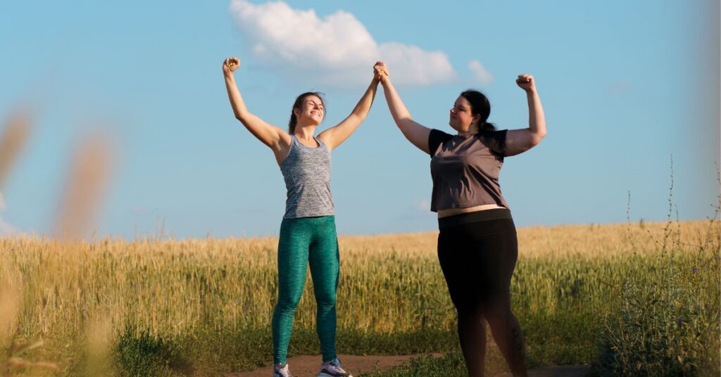 Two women of different sizes raise their arms together in celebration of achieving their SMART weight loss goals