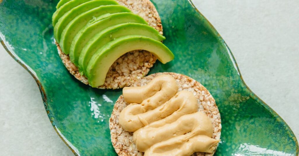 Two rice cakes, one topped with avocado slices and the other topped with hummus - weight loss snacks