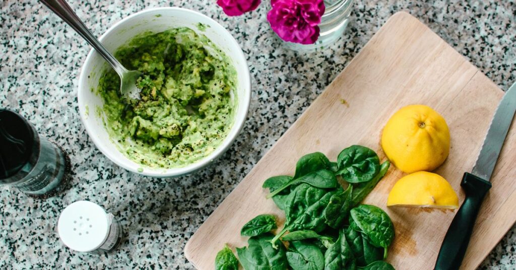 A cutting board with sliced lemon, fresh spinach, and a guacamole set aside in a bowl