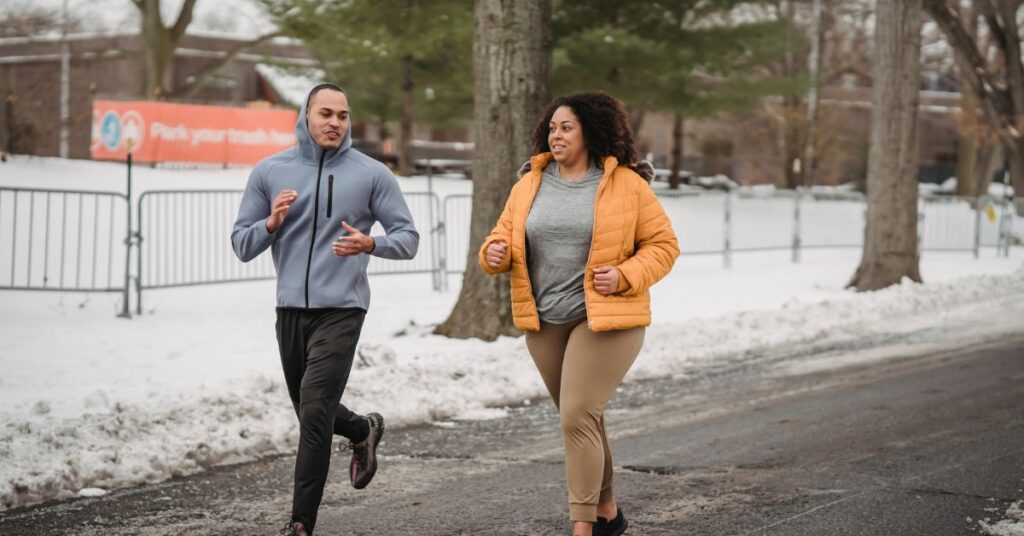 A large woman runs with a fit man outside in a snowy, winter setting, metabolism and weight loss