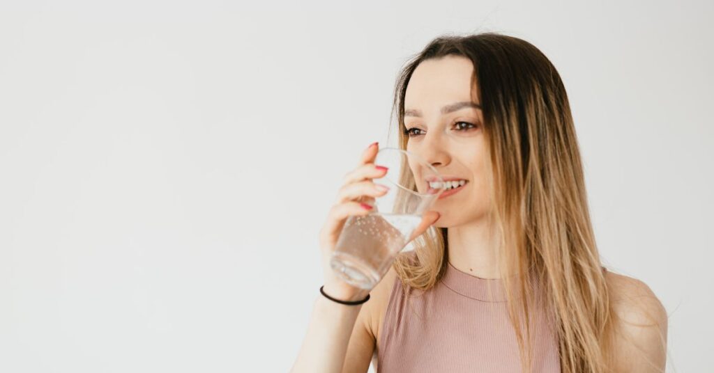 A thin woman drinks from a glass of water, metabolism and weight loss