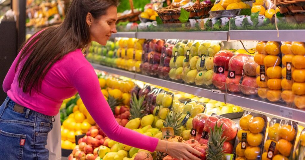 A woman in long sleeve shirt reaches for a pomegranate from her grocery store produce section, menopausal weight gain