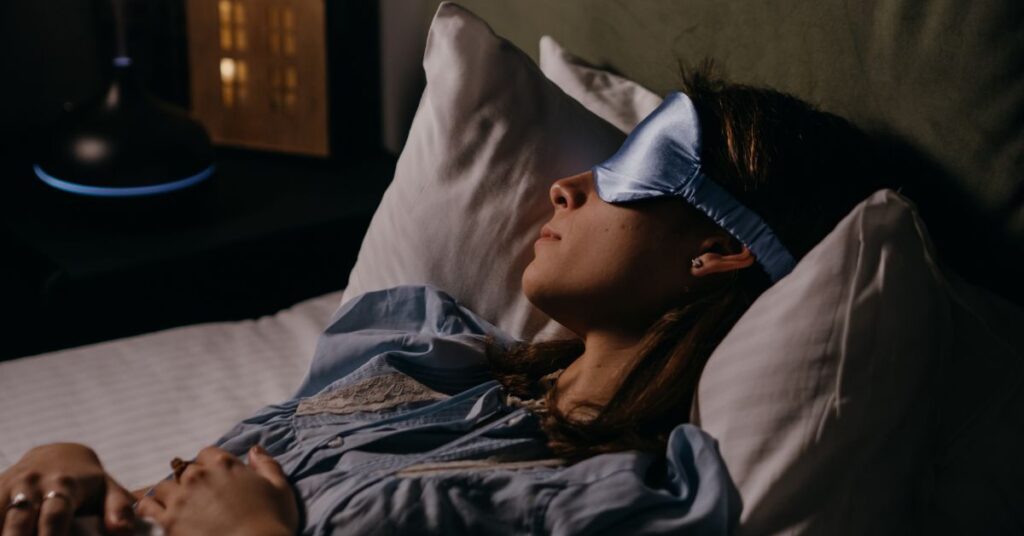 A woman with an eye mask and pajamas on, rests her head on a pillow in a dark room, menopausal weight gain