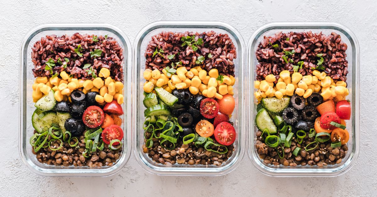 Three glass food storage containers sit in a row, each with the same meal in them of rice, lentils, corn, tomatoes, olives, and scallions, menopausal weight gain