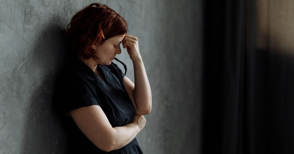 Woman leans against a wall and with her head in her hands, How to Stop Cortisol Weight Gain