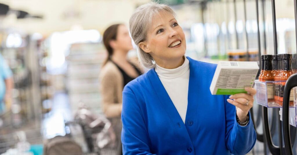 A gray-haired woman reads the labeling on a frozen box of food at the grocery store