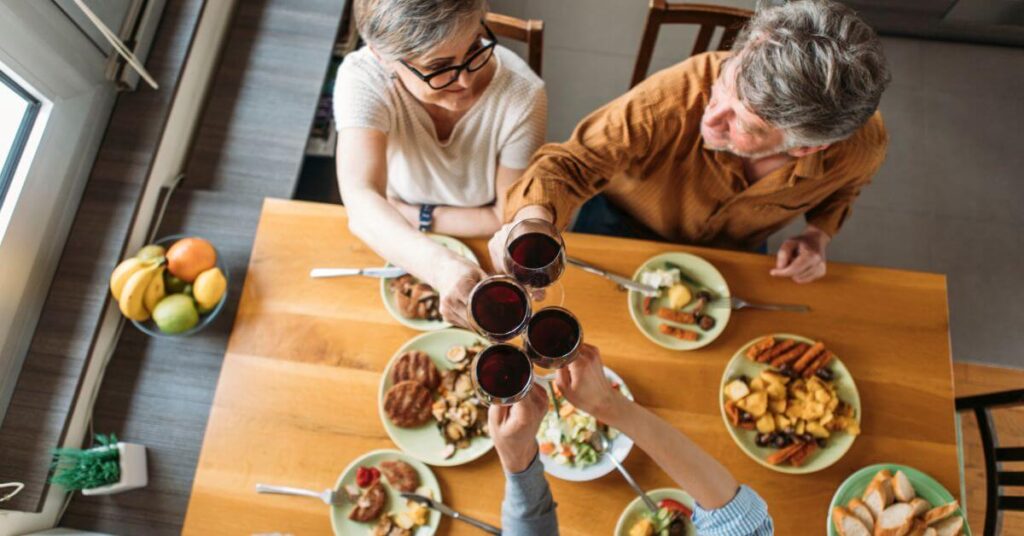 A group of gray-haired people clink wine glasses above their midday meal