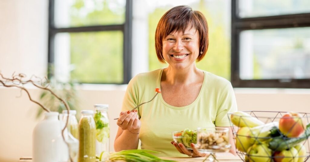 A middle aged woman happily eats a salad
