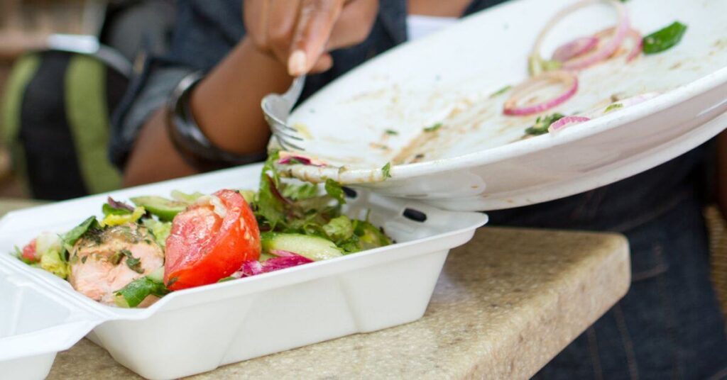 A woman scapes the leftovers of her salad into a to-go container, portion control