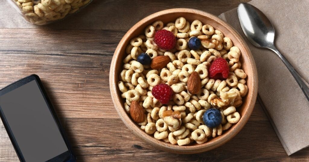 A wooden bowl filled with cheerios and topped with raspberries, blueberries, almonds and walnuts, portion control for weight loss