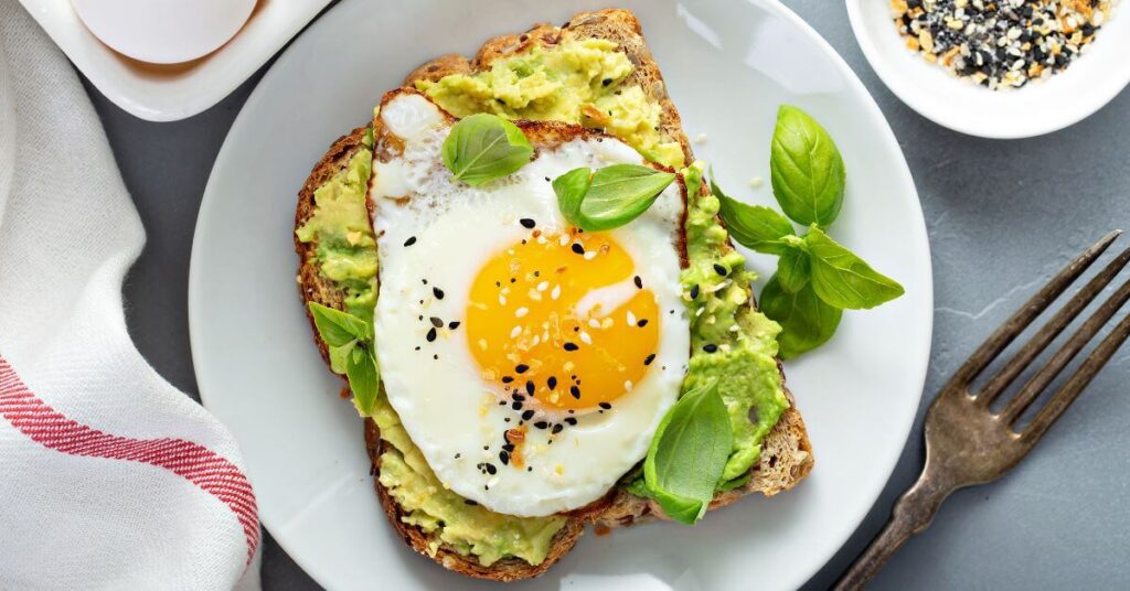 A brightly lit photo of toast slathered in smashed avocado and topped with a sunny side up egg and fresh basil, long term weight loss management