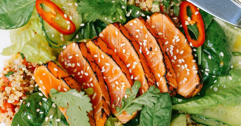 A close up of seared slices of salmon, a healthy fat, laid on top of a herb, lettuce and quinoa salad