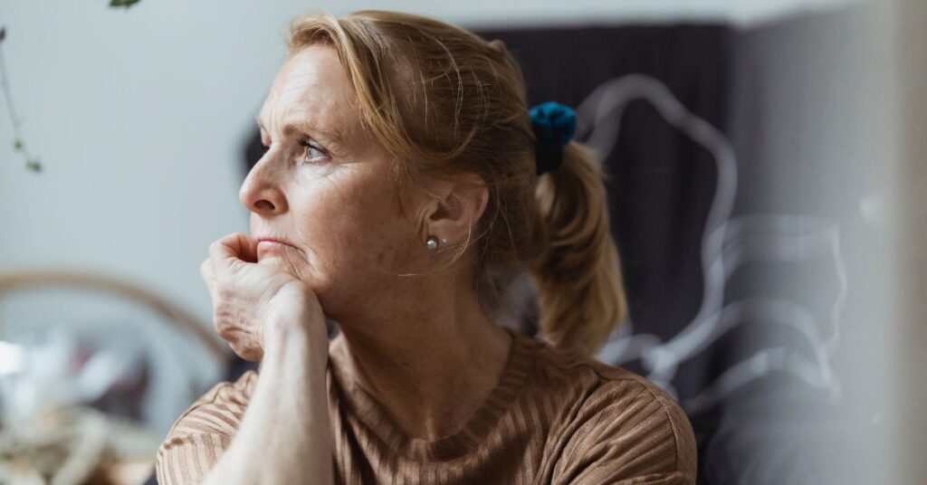 A middle-aged woman holds her hand up to her chin and looks off into the distance in a moment of reflection