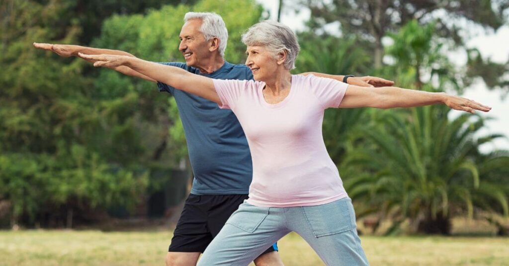 A white-haired couple do a warrior two yoga pose in an outdoor setting, long term weight loss management