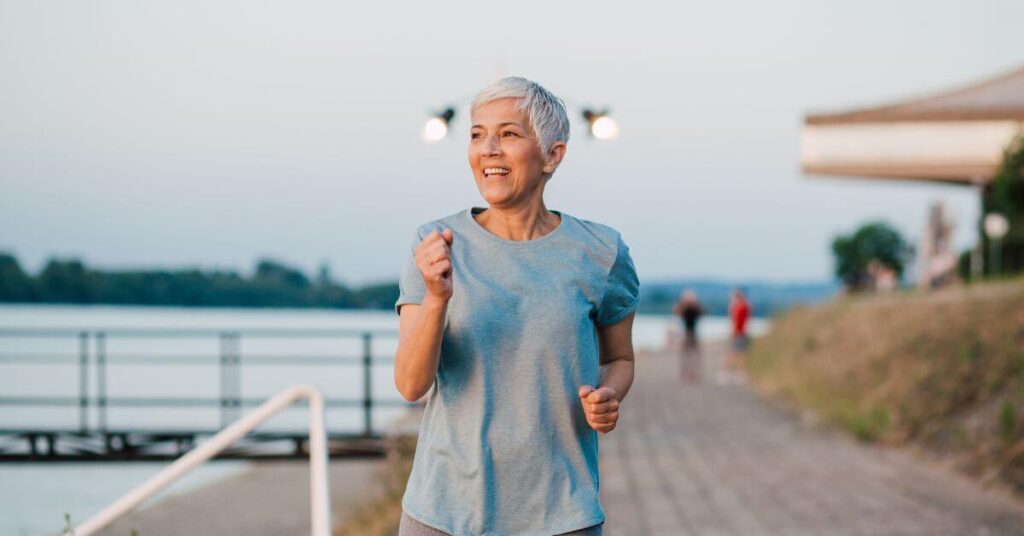 A white-haired woman with a pixie cut runs along a coastal walkway and smiles