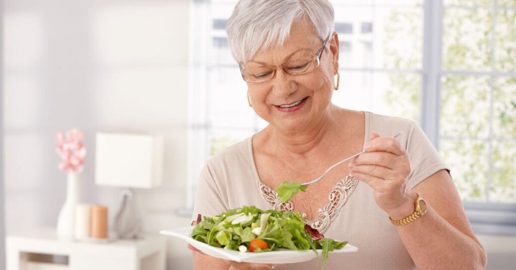A white haired woman with thin rectangular glasses and a pixie cut takes a bite of a salad, long term weight loss management