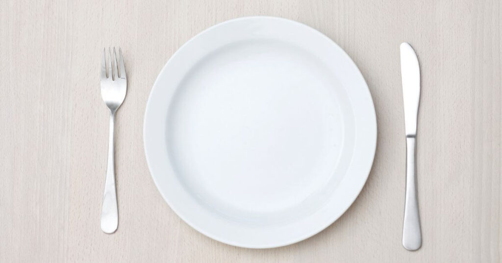 An empty plate sits on a tabletop with a fork and knife set on either side, long term weight loss management