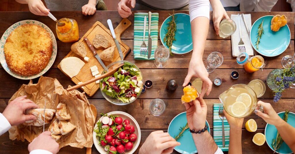 An overhead view of a dinner table with salad, bread and lemonade all being passed around