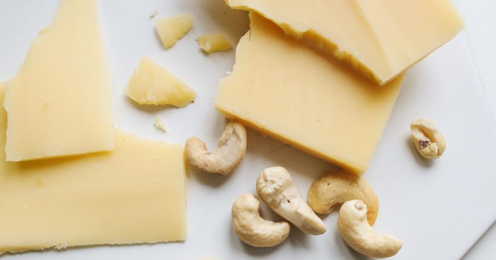 Chunks of a hard cheese and salted cashews are haphazardly placed on a cutting board, healthy fats