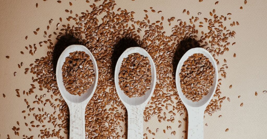 Three wooden spoons lined up in a row, each holding flaxseeds, healthy fats