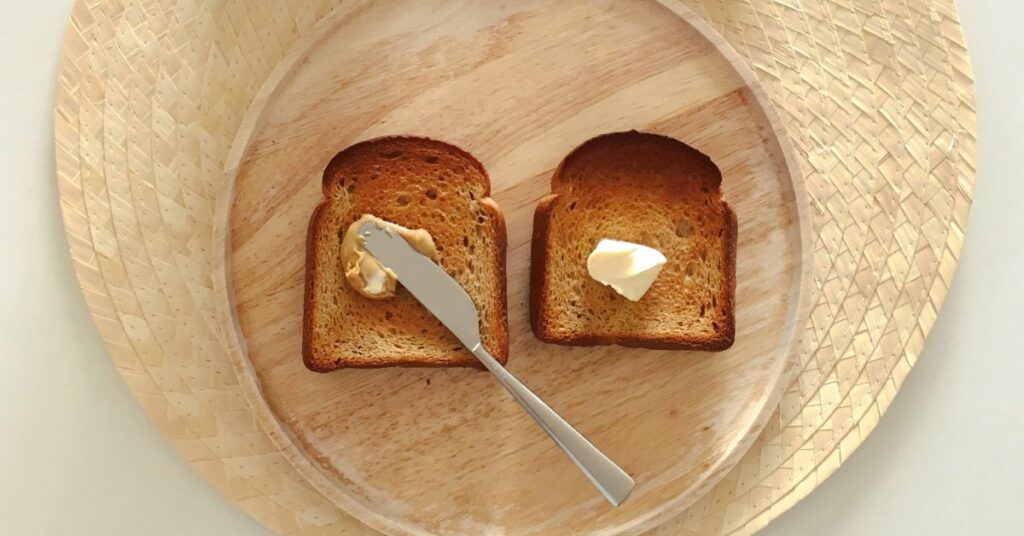 Two slices of toast topped with a dollop of butter rest on a wooden plate