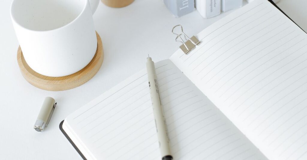 A blank lined journal with a thin point marker pen laying on top and a coffee mug next to it, mindful eating journal