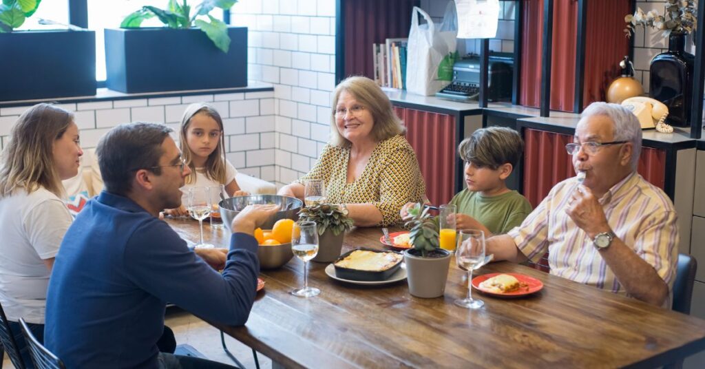 A family of children, parents and grandparents sit around a dinner table before their meal, mindful eating