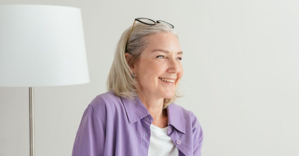 A white haired woman with glasses on her head looks off into the distance and smiles