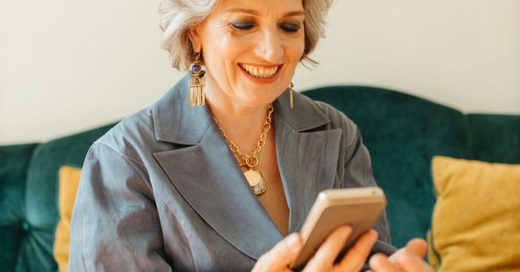 An older female with chunky gold jewelry smiles as she looks at her cellphone