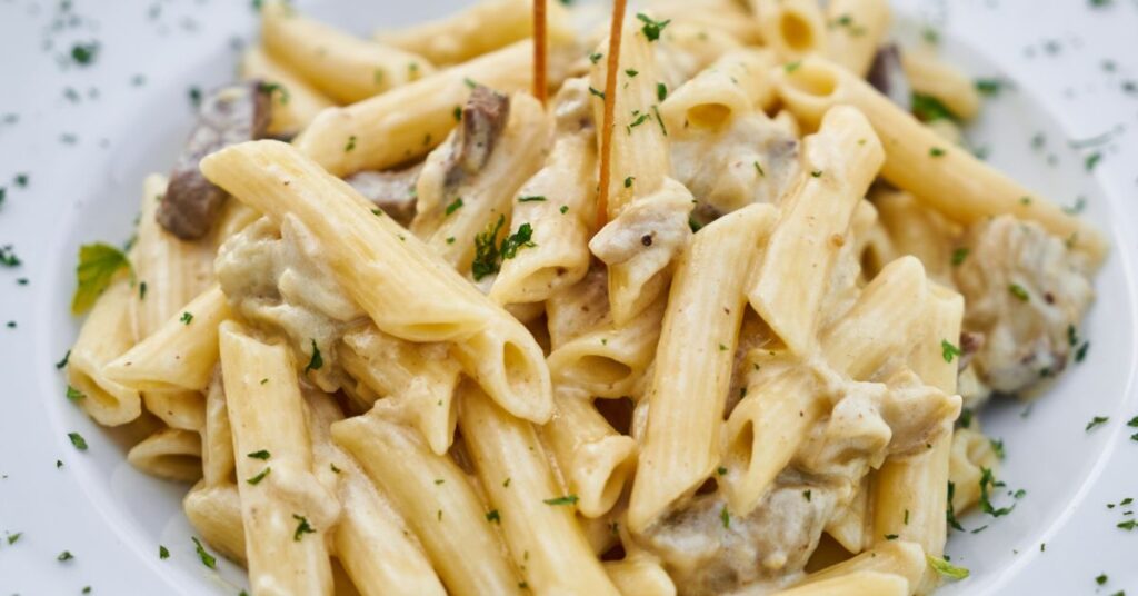 Plate of ziti noodles with a cream sauce, mushrooms and herbs topping it