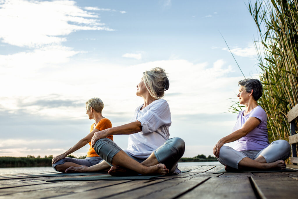 group of women doing yoga exercises outside on a dock by a lake or river