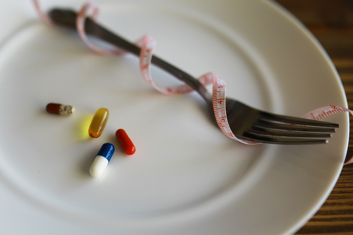 fad diets medical weight loss concept - fork and pills on an empty place