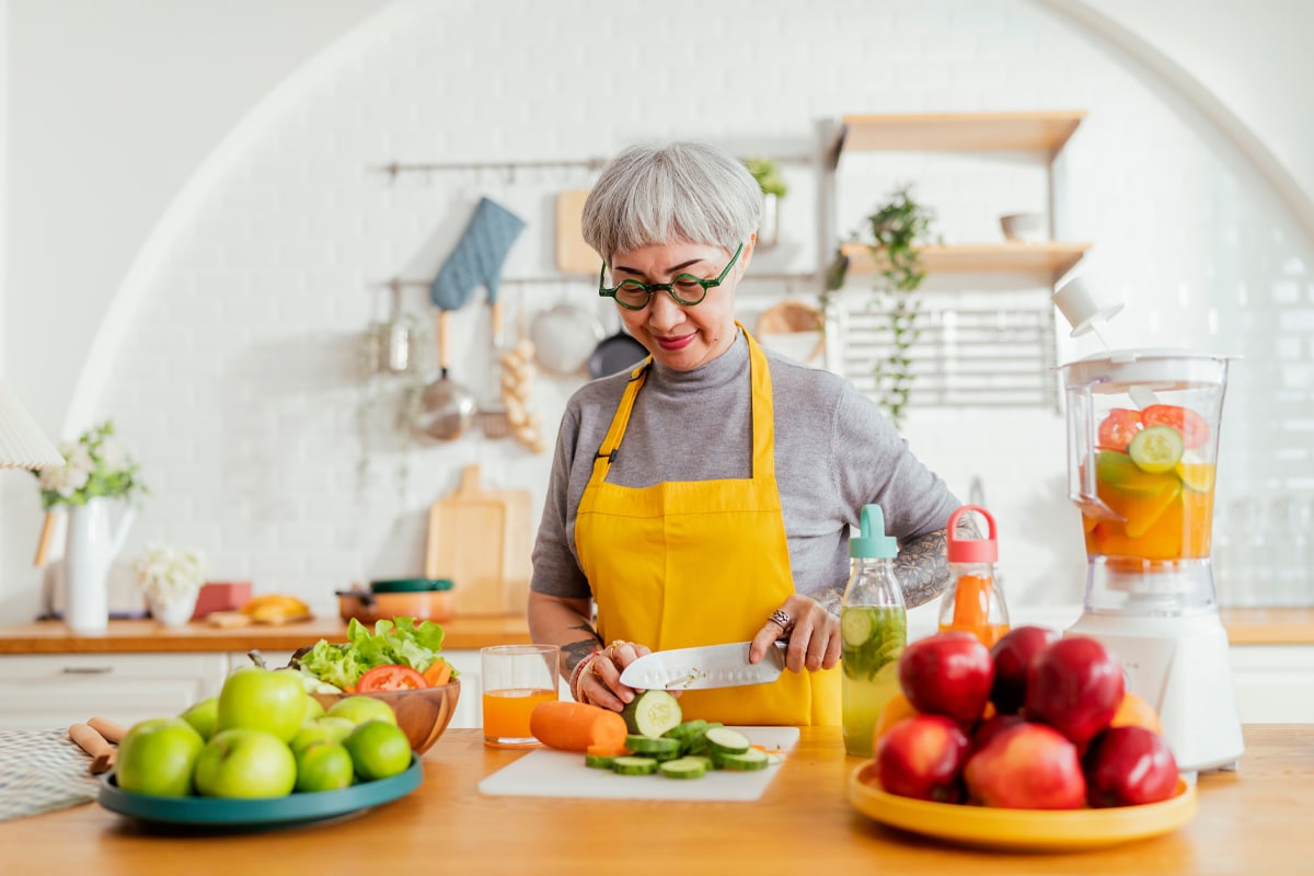 woman chopping vegetables in the kitchen next to bowls of apples