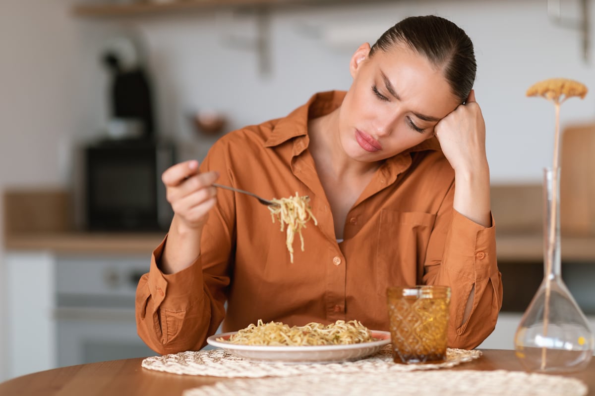 emotional eating - woman sitting at a table alone sad eating pasta
