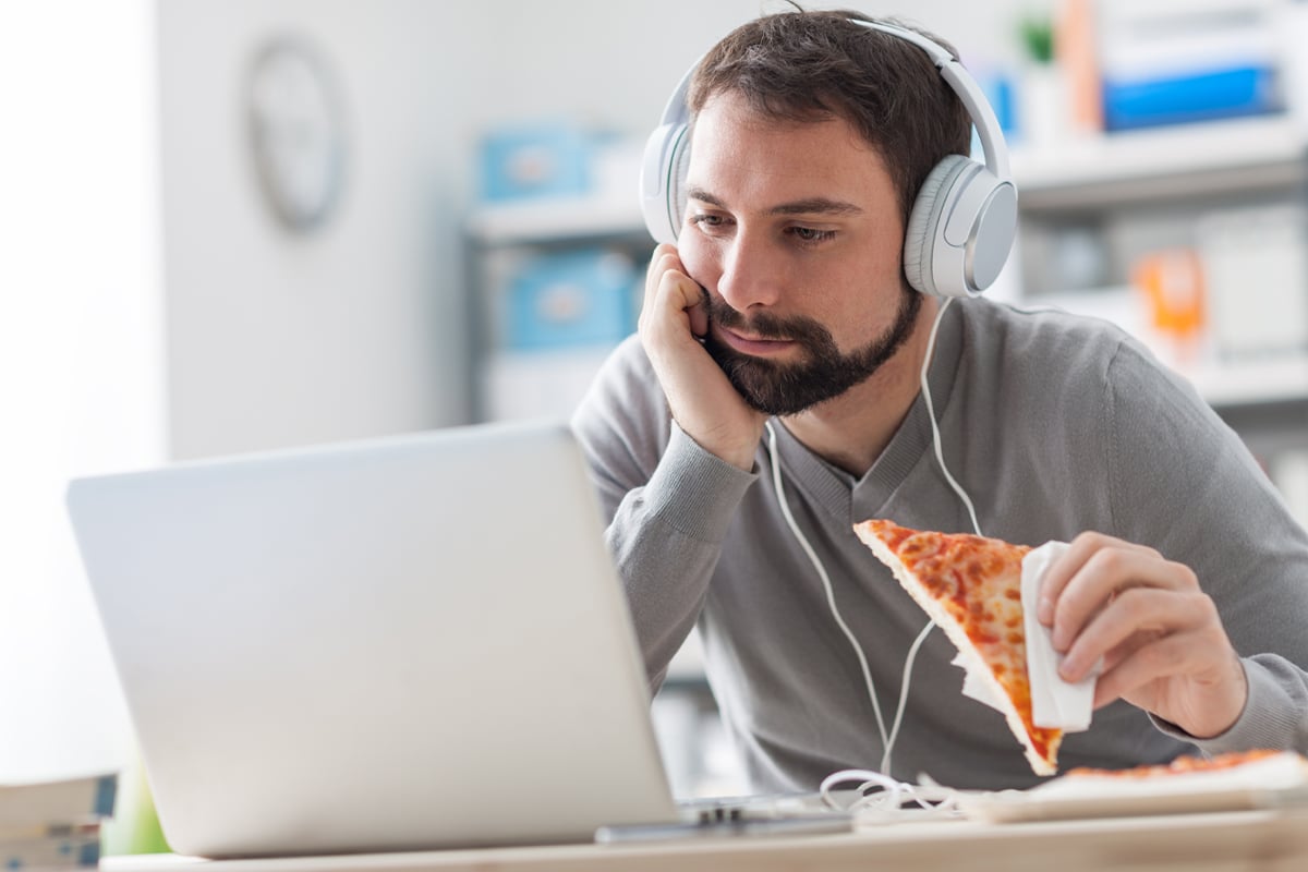 stressed out man eating a pizza at his computer while working